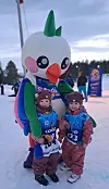 To barn i Coop-startnummer smiler sammen med maskoten Snedi på snødekt stadion.
