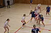 Håndballspillere i hvitt og blått i tett duell nær målfeltet i en idrettshall.