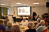 Eldre deltakere følger et foredrag i et lyst møterom med projektor