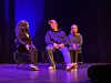 Tre personer sitter på stoler på en mørk scene med blått scenelys.
