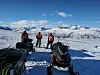 Personer ved snøscootere på snødekt fjellplatå med fjell i bakgrunnen