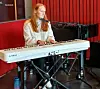 Musiker sitter ved hvitt Kawai-keyboard og synger i mikrofon i studio