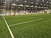 Innendørs fotballhall med barn som spiller på kunstgressbane foran et mål.
