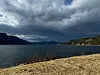 Fjord med fjell i bakgrunnen under mørke skyer sett fra tørr gresslette.