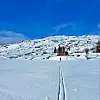 Skitrasé i dyp snø som leder mot en rød hytte i solfylt vinterfjell