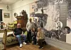 Fire personer i museumstue foran stor Talgo-vegg med historiske bilder.