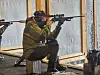 Sittende skytter med rifle sikter fremover på innendørs bane.