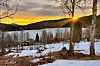Snødekt dal med gårdshus og bjørketrær i solnedgang