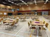 Idrettshall med oppstilte bord og stoler klare for arrangement