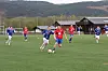 Fotballspillere i røde og blå drakter løper mot ballen på en utendørs kunstgressbane.