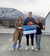 Tre personer holder en stor SpareBank 1-sjekk foran snødekt fjell