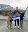 Tre personer holder en stor SpareBank 1-sjekk foran snødekt fjell