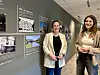 To personer står i korridor foran vegg med historiske fotografier og tekstplakater.
