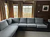 Grå hjørnesofa i trepanelt stue foran store vinduer med gardiner