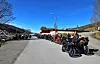 Rekke motorsykler parkert langs landevei ved bygg på solrik dag