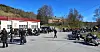 Flere motorsykler parkert foran verkstedbygg med folk som samles utendørs