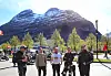 Motorsyklister står parkert foran et høyt, snødekt fjell på en solrik dag
