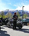 Motorsyklist står ved flere motorsykler på parkeringsplass foran snødekte fjell.