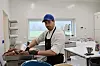 Kokk i hvit jakke og blå caps står ved en kvern med kjøtt i et lyst kjøkken.
