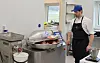 Kokk i blå caps står ved en stor metallgrill i et kjøkken med matvarer og redskaper.