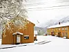 Snødekt gårdsplass med trebygninger, norske flagg og fjell i bakgrunnen.