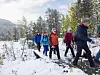 Flere personer går på en snødekt skogssti med fjell i bakgrunnen.