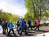 En gruppe personer går på en grussti ved trær og snøflekker en solrik dag.