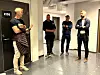 Fire menn står i en lys kontorgang ved en dør merket K108.