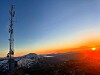 Solnedgang over fjell med en høy telemast i forgrunnen.