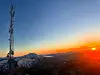 Solnedgang over fjell med en høy telemast i forgrunnen.