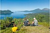 Tre personer sitter på en åsrygg med utsikt over fjord, øyer og fjell under blå himmel.