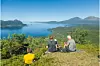 Tre personer sitter på en åsrygg med utsikt over fjord, øyer og fjell under blå himmel.
