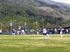 Fotballspillere i kamp på en gressbane foran fjell og skog.