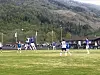 Fotballspillere i kamp på en gressbane foran fjell og skog.