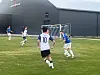 Fire fotballspillere i aksjon på en gressbane foran en stor mørk bygning.