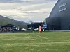 En fotballspiller i oransje drakt på en gressbane foran en stor tribune og fjell.