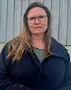 Kvinne med briller og langt hår foran en lys grå trevegg.