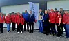 Gruppe i røde jakker står foran en bygning med banner og store porter.