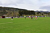 Fotballspillere på en grønn bane med skog og fjell i bakgrunnen.