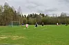 Spillere på en fotballbane med mål og trær i bakgrunnen.