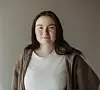 Portrett av en kvinne i hvit topp og brun cardigan foran en nøytral vegg.