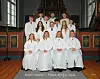 Konfirmanter i hvite drakter poserer foran alteret i en kirke.