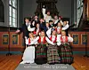 En korgruppe poserer foran et orgel i en kirke, med tradisjonelle drakter og festklær.