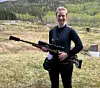 En person står på en utendørs skytebane og holder en rifle foran seg.