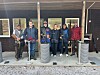 Seks skyttere står foran en trebygning med søyler og utstyr på standplass på en leirduebane.