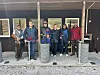 Seks skyttere står foran en trebygning med søyler og utstyr på standplass på en leirduebane.