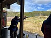 Personer skyter fra en overbygd standplass mot leiirduer i et åpent landskap.