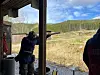 Personer skyter leirduer fra en overbygd stand på en utendørs skytebane.
