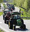 En rekke traktorer kjører tett etter hverandre på en svingete vei omgitt av grønt landskap.