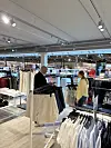 To personer står mellom klesstativer i en lys, moderne klesbutikk.